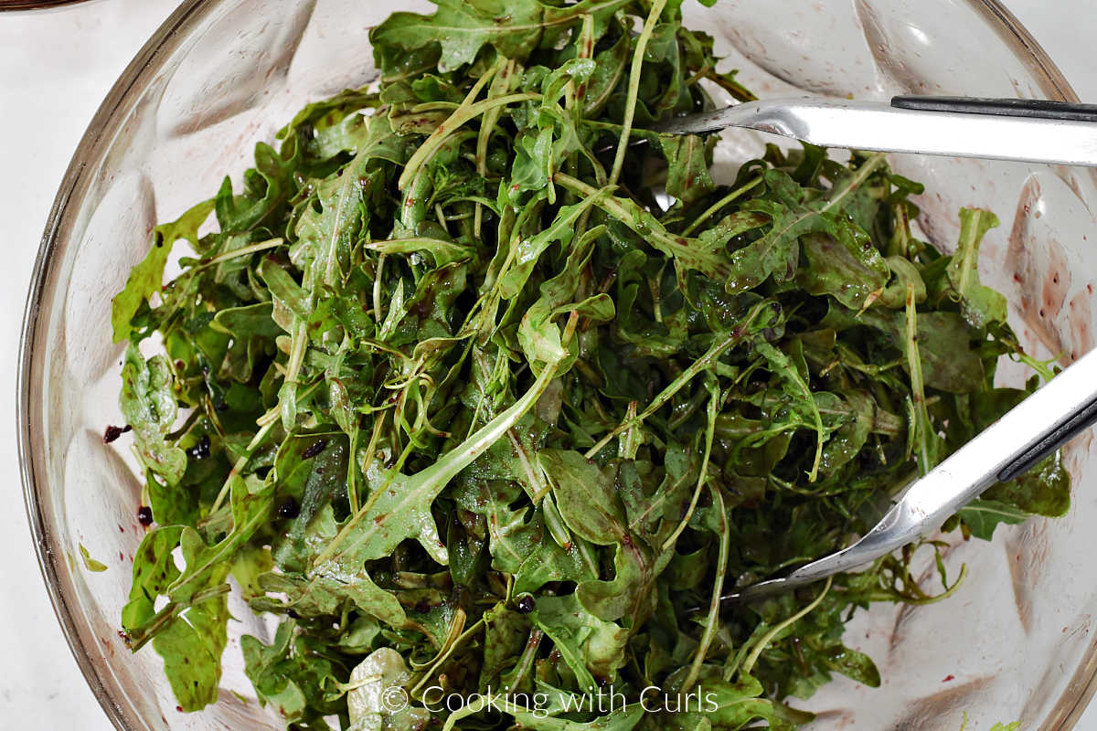 Arugula leaves tossed with blueberry vinaigrette in a large bowl.