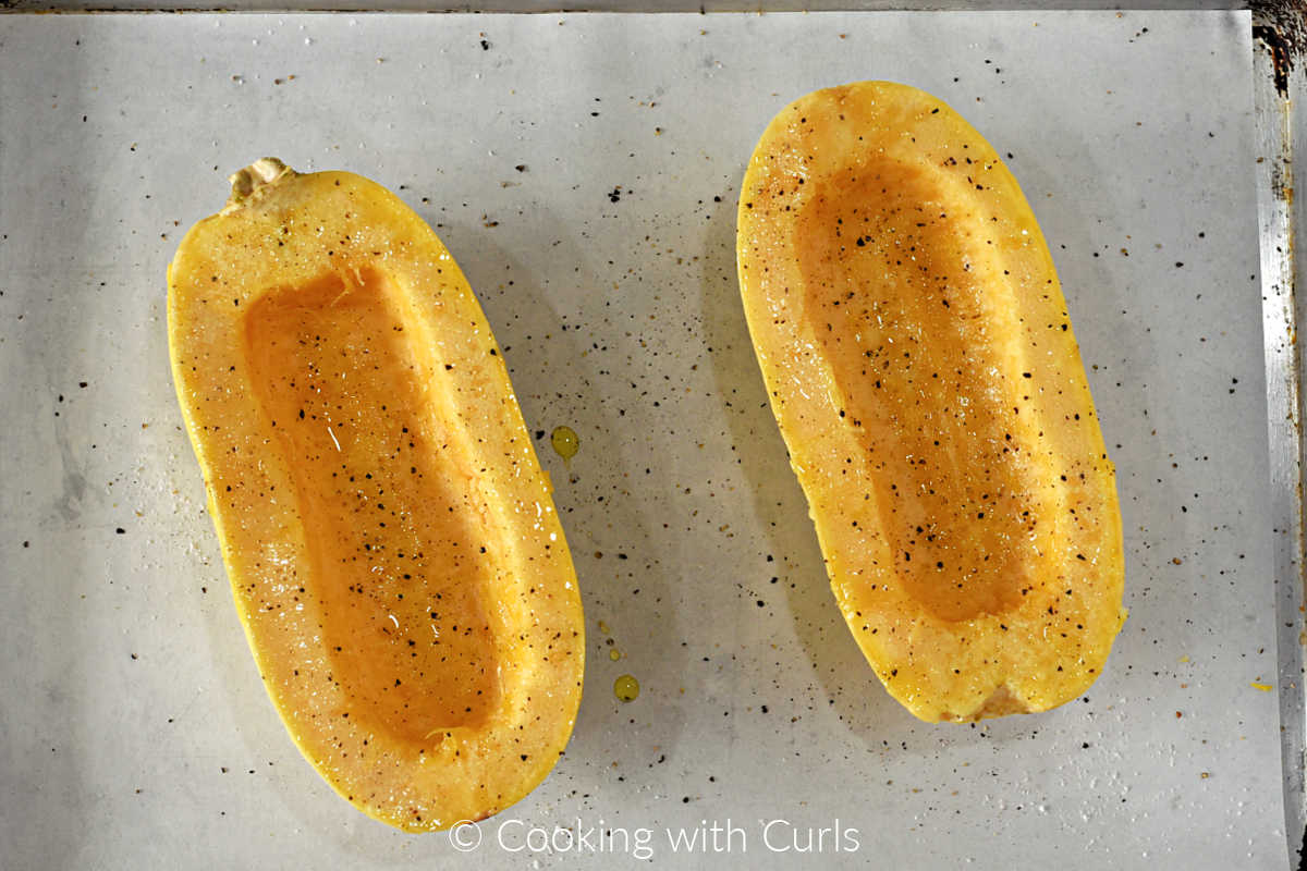 Seasoned spaghetti squash halves on a parchment lined baking sheeet.