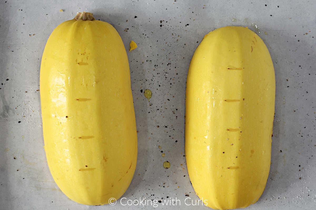 Spaghetti squash halves upside down on parchment lined baking sheet.