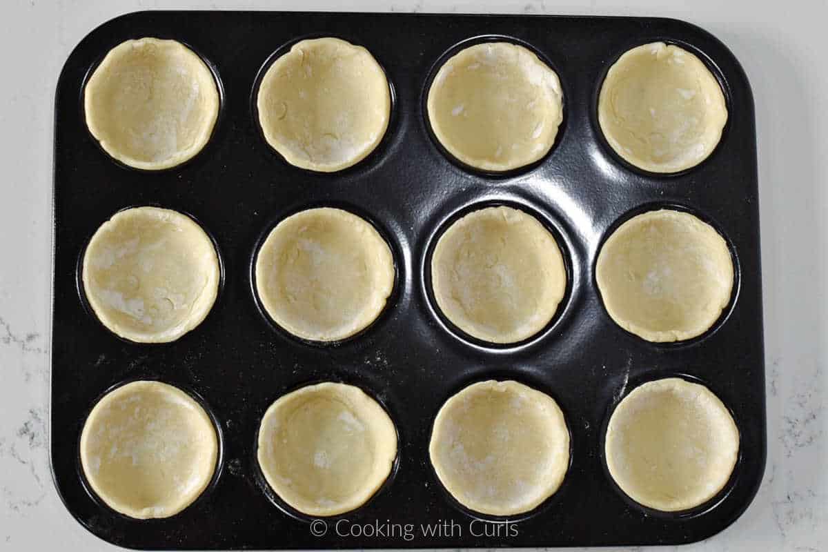 Twelve puff pastry circles in a mini tart pan.