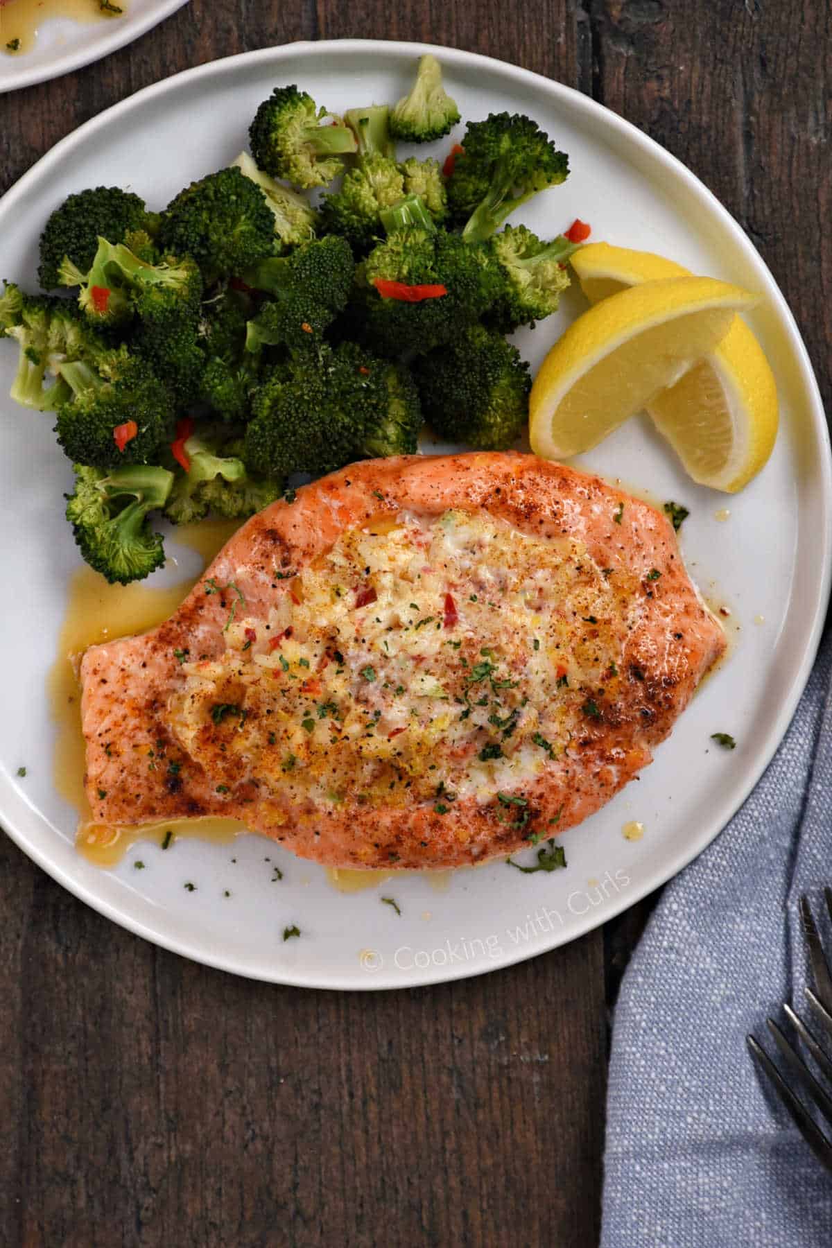 Salmon with crab filling on a plate with steamed broccoli and lemon wedges.