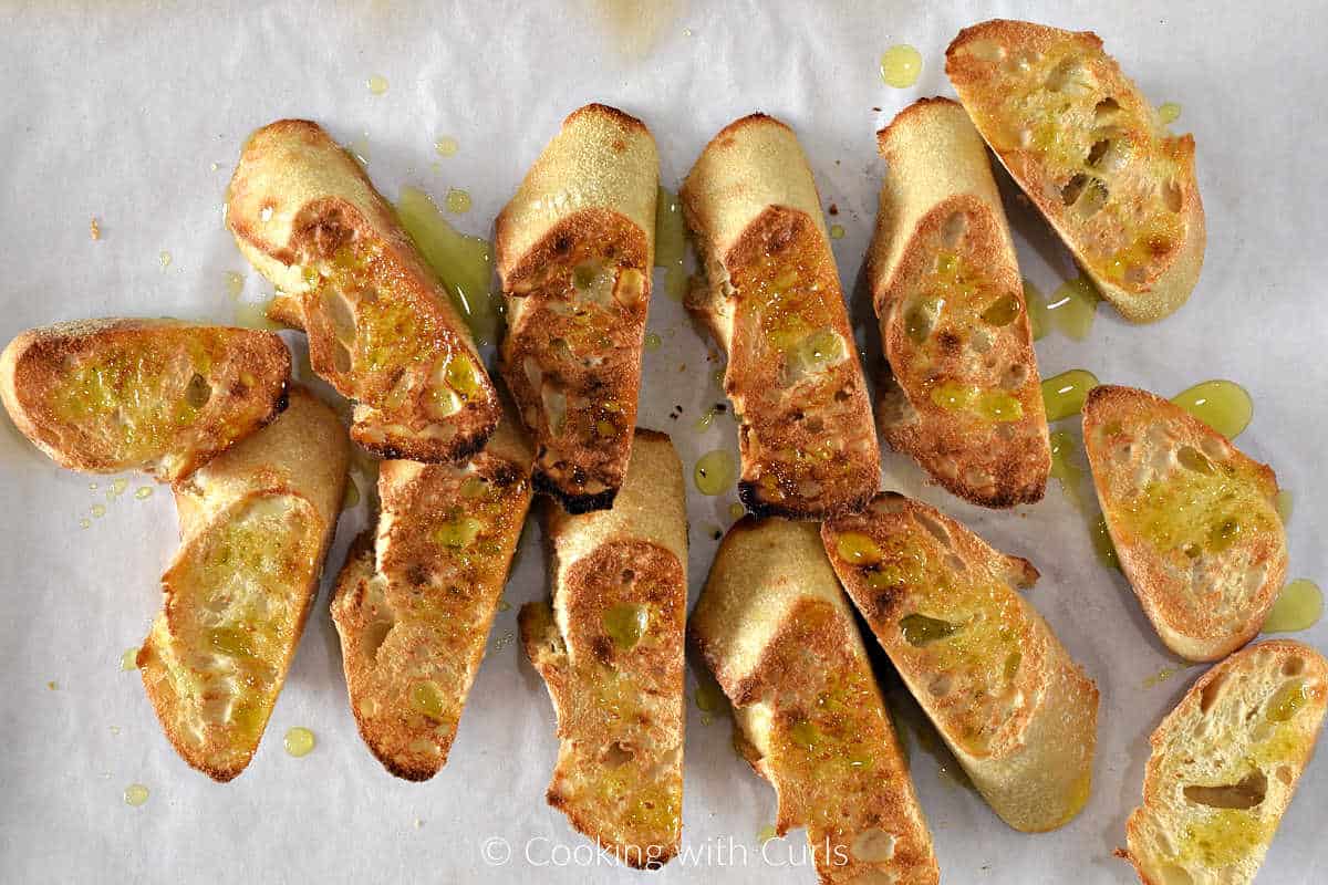 Toasted bread slices with garlic and olive oil on baking sheet.