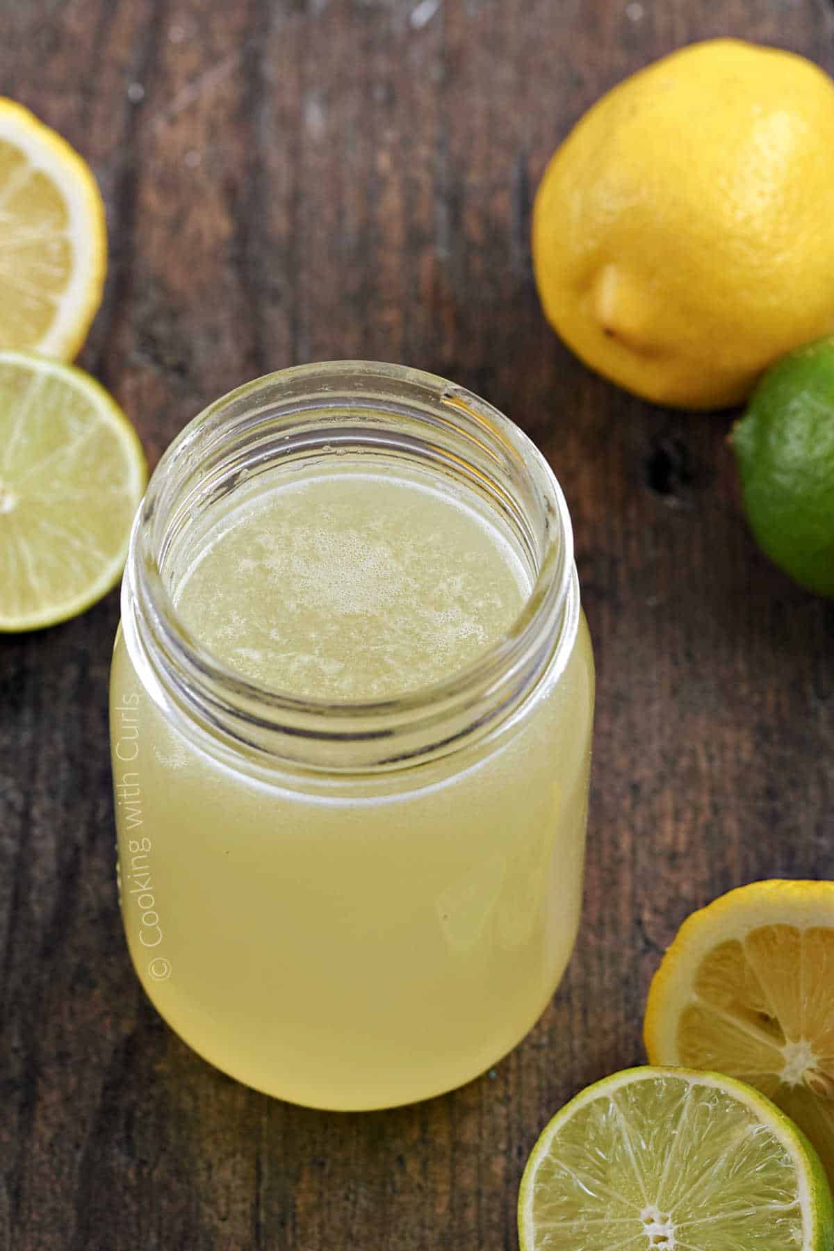 Sweet and sour mix in a mason jar surrounded by lemons and limes.