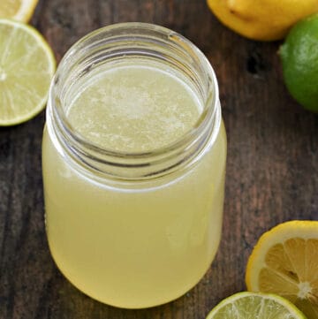 Sweet and sour mix in a mason jar surrounded by lemons and limes.