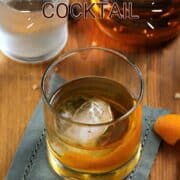 Classic Old Fashioned cocktail in a rocks glass with an ice ball and orange twist with title graphic across the top.