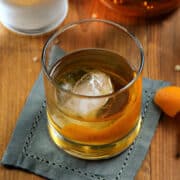 Classic Old Fashioned cocktail in a rocks glass with an ice ball and orange twist.