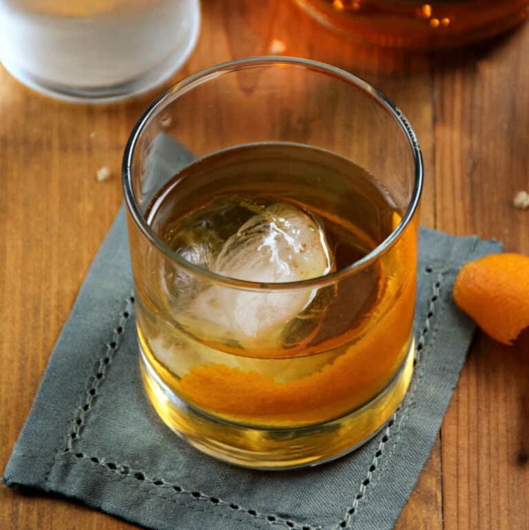 Classic Old Fashioned cocktail in a rocks glass with an ice ball and orange twist.