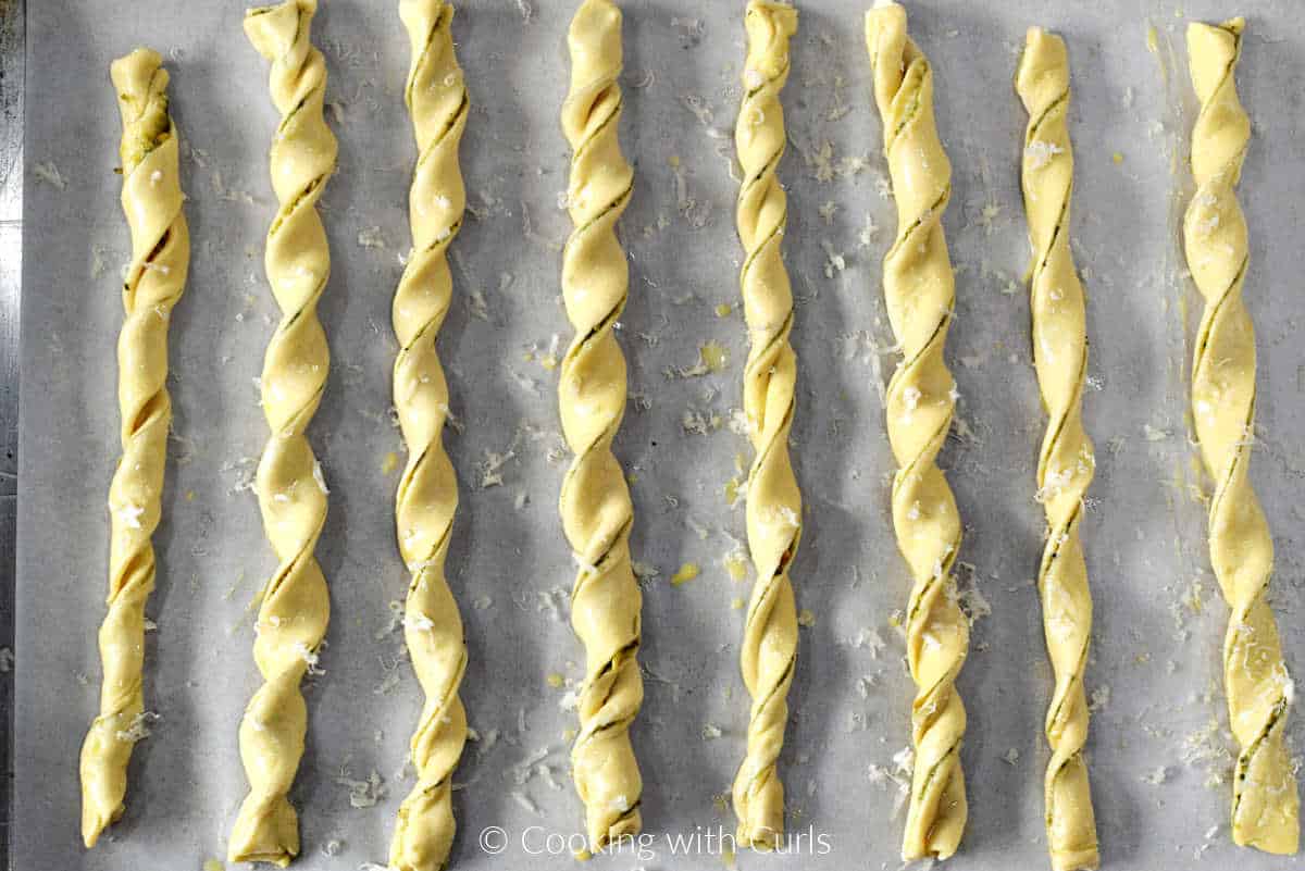 Eight pesto puff pastry twists on a parchment lined baking sheet.