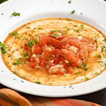 A bowl of cheesy grits topped with seasoned shrimp and parsley.