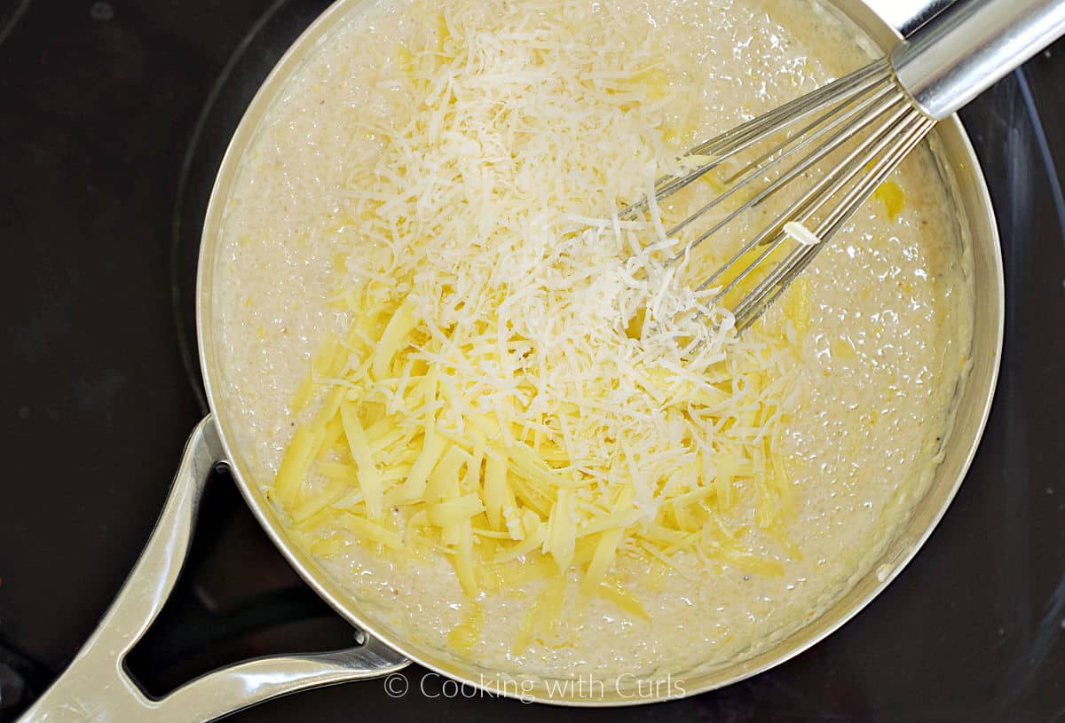 A pan of grits with grated cheese and butter with a whisk resting on the edge.