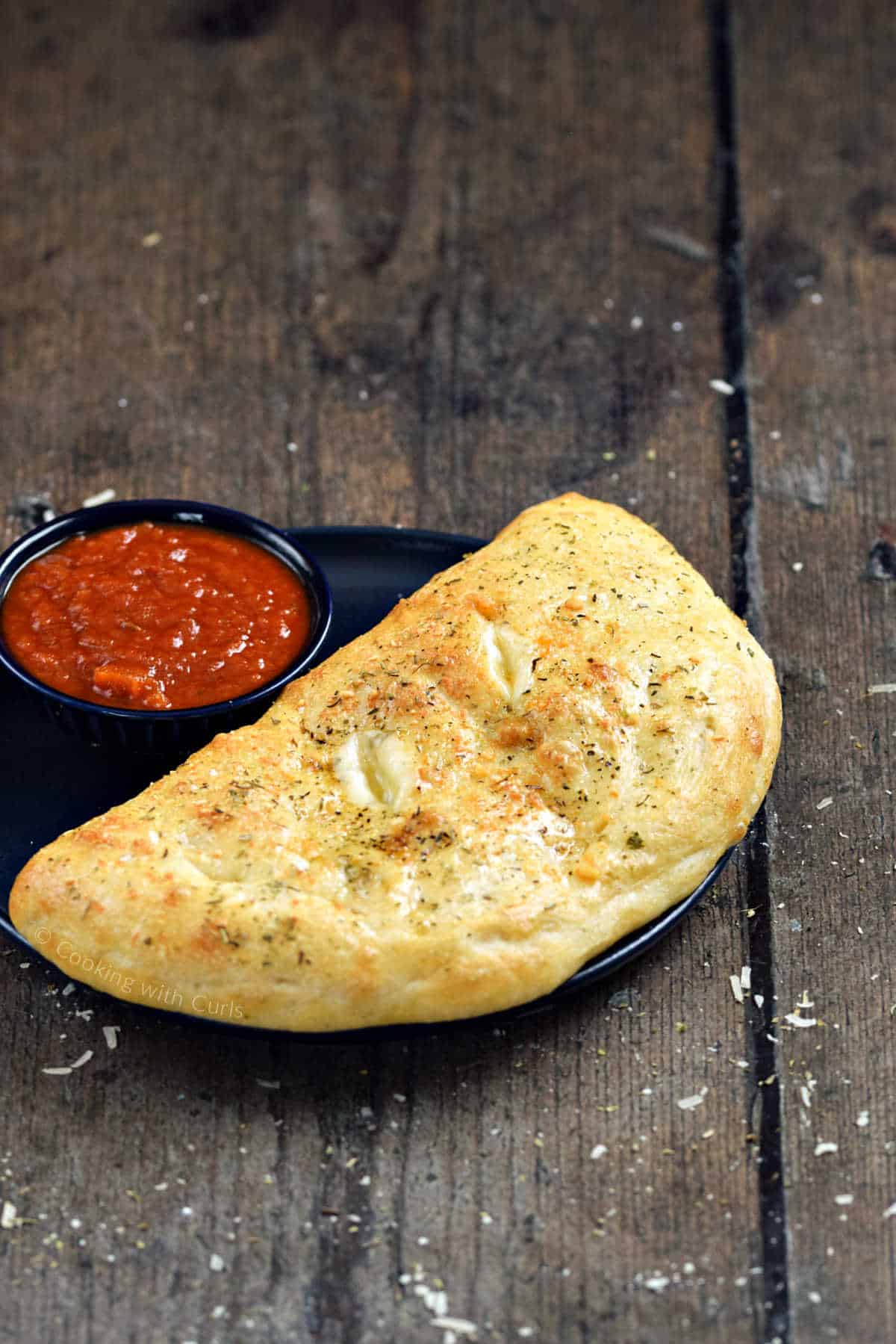 Baked calzone on a plate with small bowl of pizza sauce on the side.