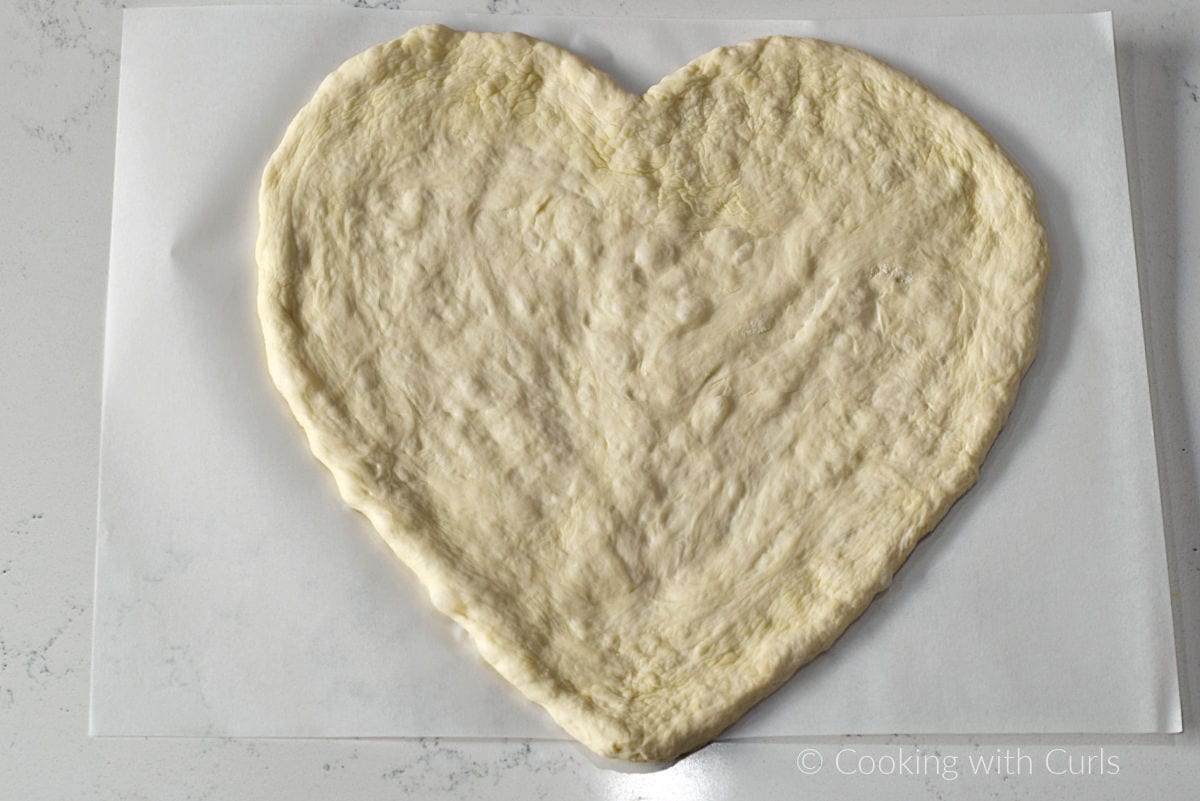 Heart shaped pizza dough on parchment paper.