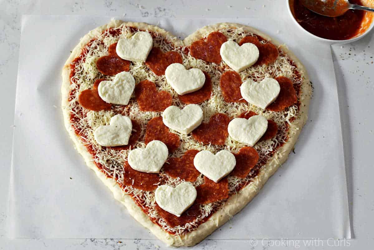 Heart shaped pizza dough topped with sauce, heart shaped pepperoni and mozzarella cheese.