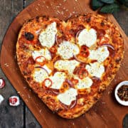 Heart shaped pizza with pepperoni hearts on a wood pizza peel.