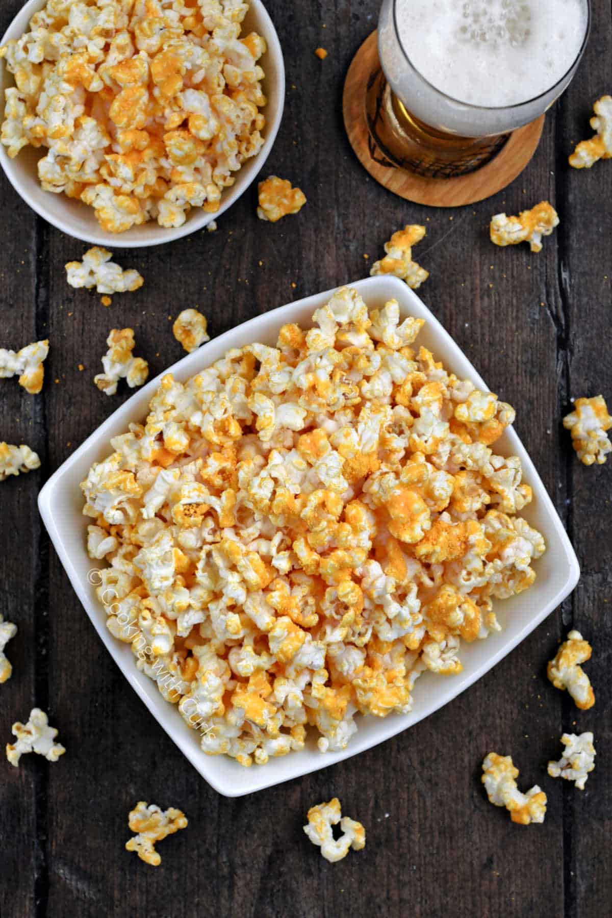 Two bowls of cheddar cheese popcorn surrounded by scattered pieces of popcorn.