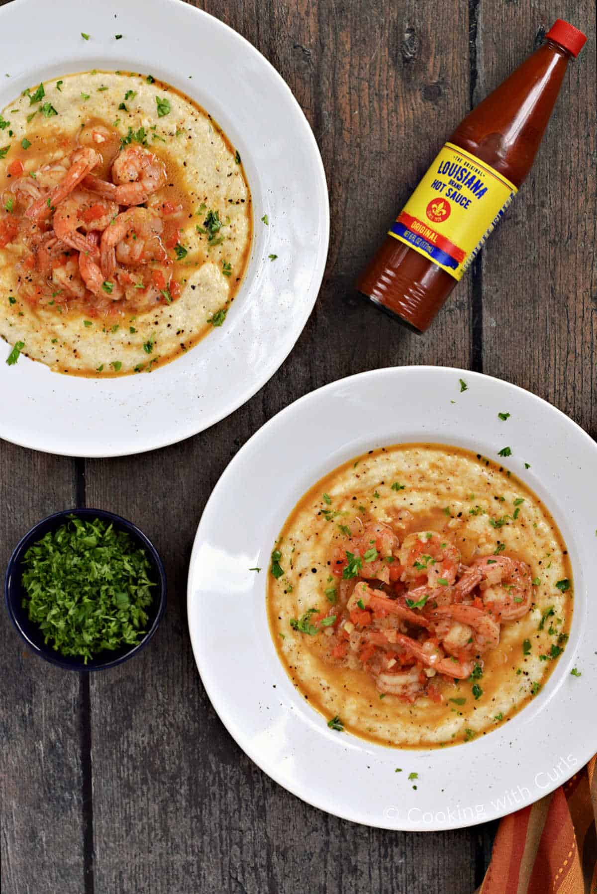 Two bowls of cheesy grits topped with seasoned shrimp and sprinkled with parsley.