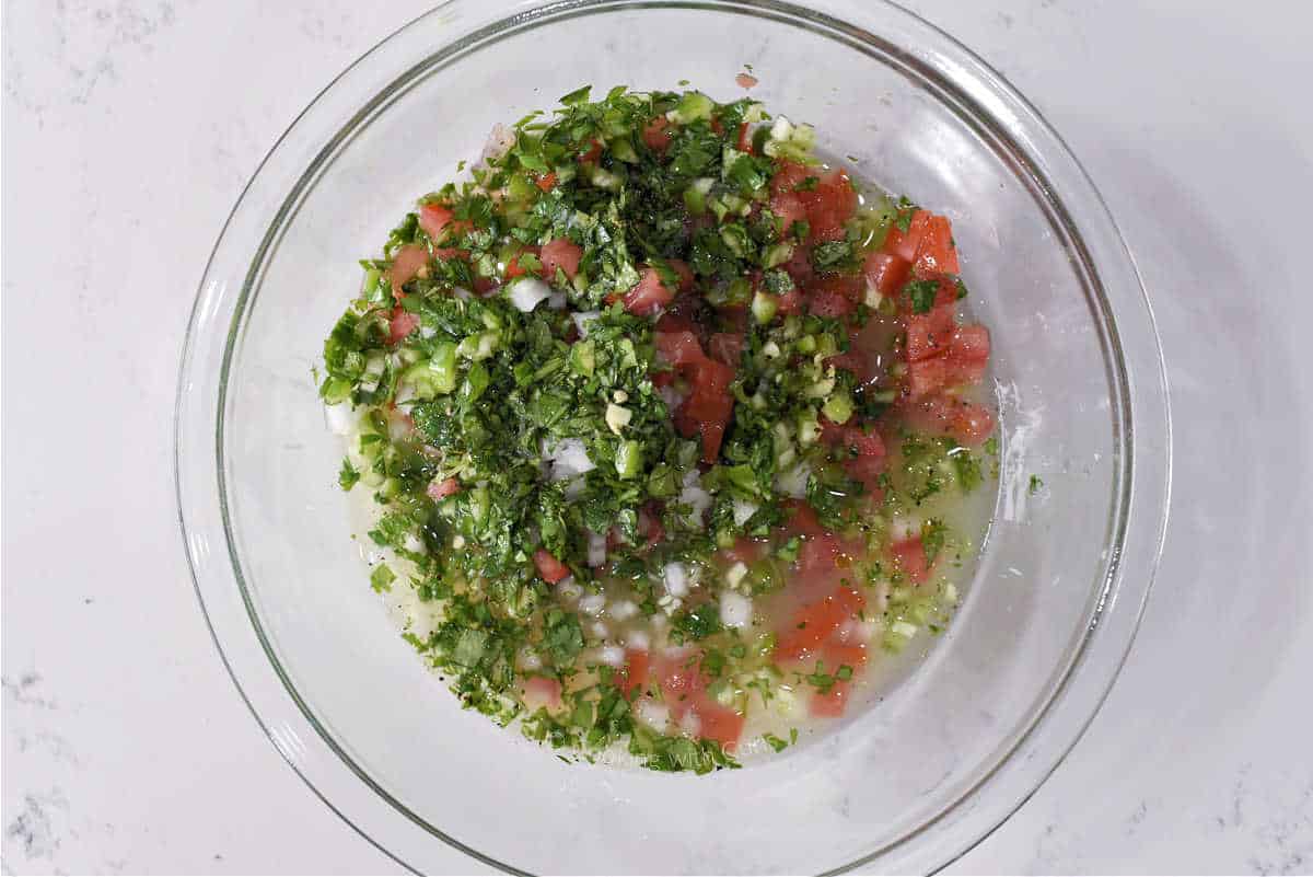 Chopped cilantro, serrano pepper, tomato, and onion with lime juice in a glass bowl.