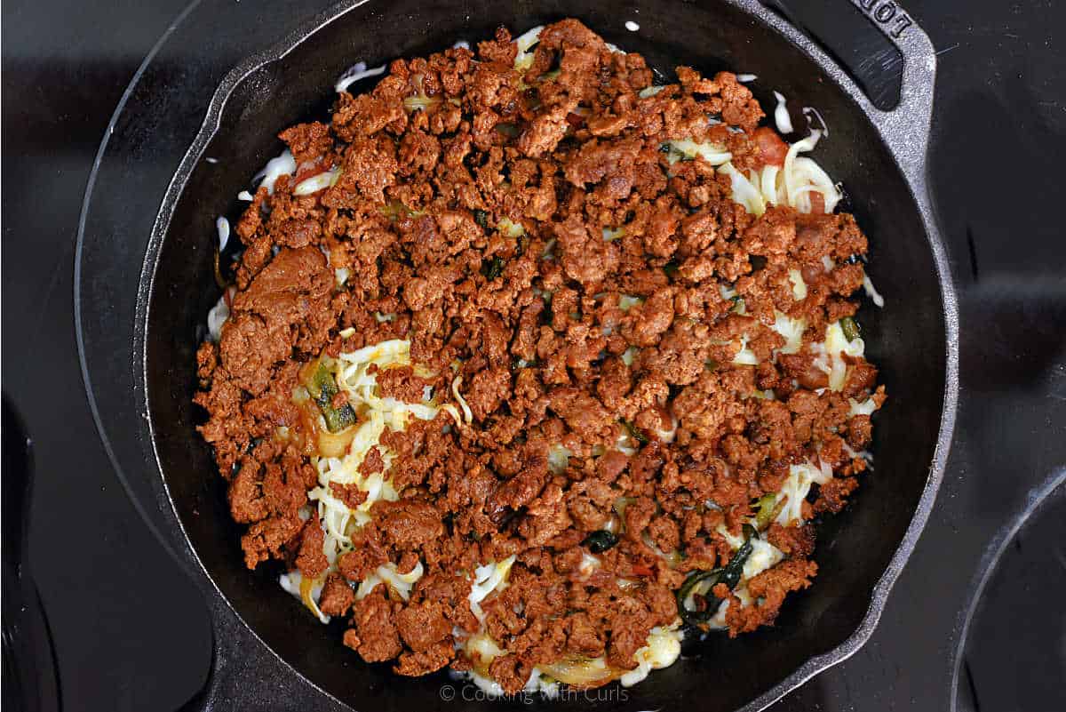 Chorizo sausage over cheese and pepper mixture in skillet.