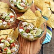 Shrimp, tomato, avocado, and peppers in small bowls surrounded by tortilla chips.