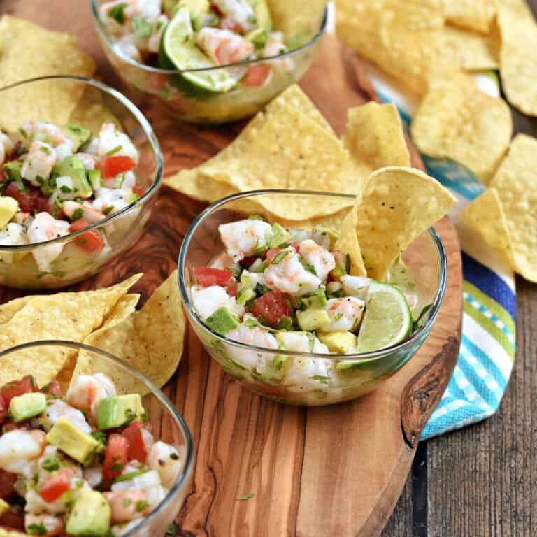 Shrimp, tomato, avocado, and peppers in small bowls surrounded by tortilla chips.