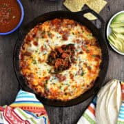 Melted cheese and chorizo dip in a cast iron skillet with tortilla chips and salsa in bowls.