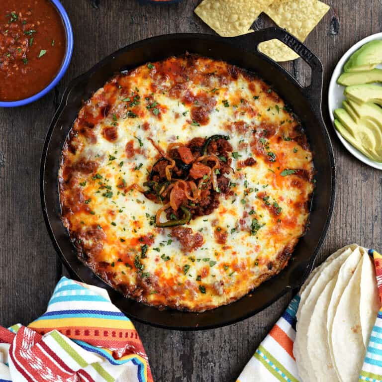 Melted cheese and chorizo dip in a cast iron skillet with tortilla chips and salsa in bowls.