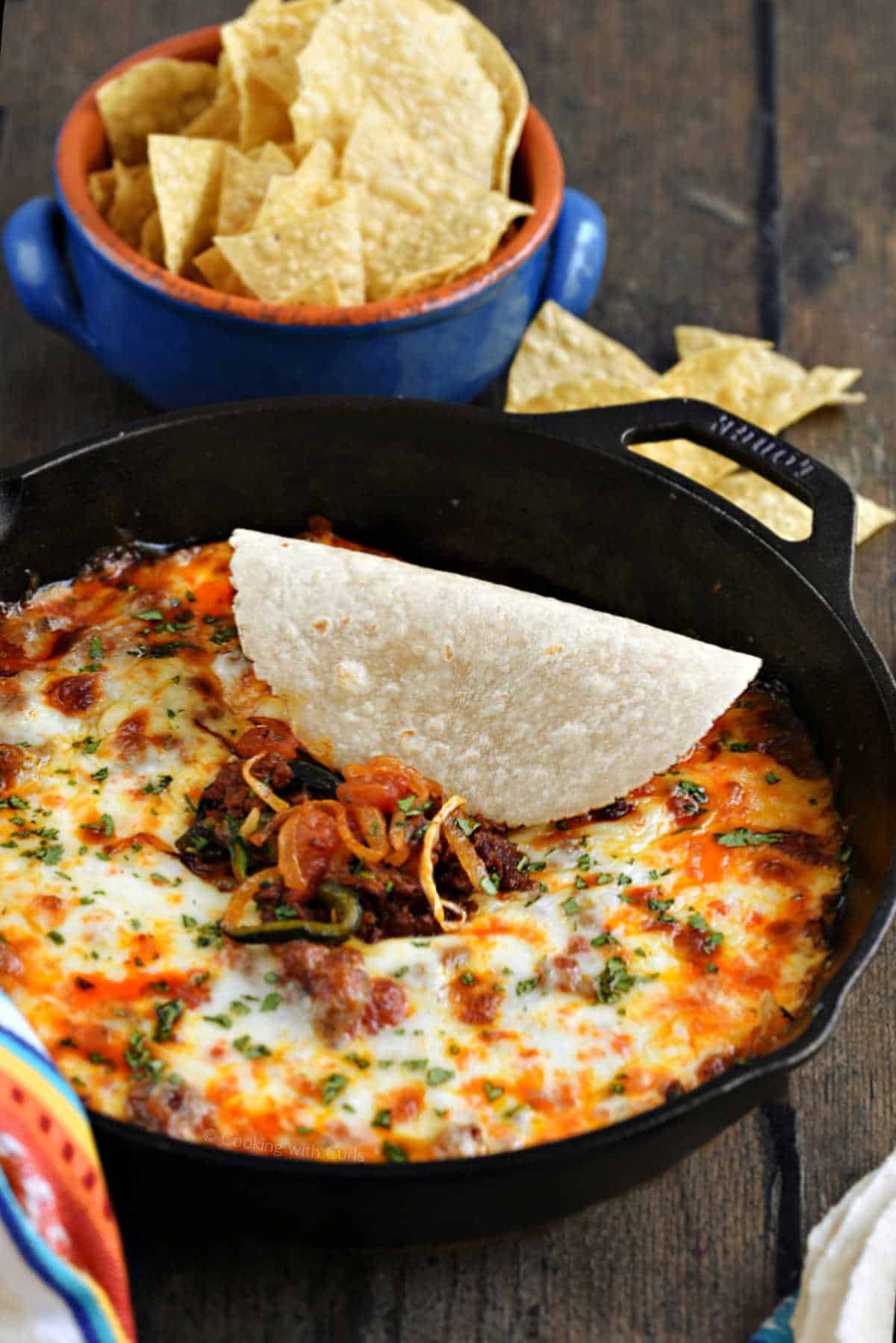 Queso fundido in skillet with small tortilla scooping up the dip.