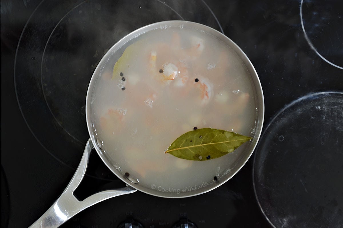 Saucepan with hot water, bay leaves, shrimp, and peppercorns.