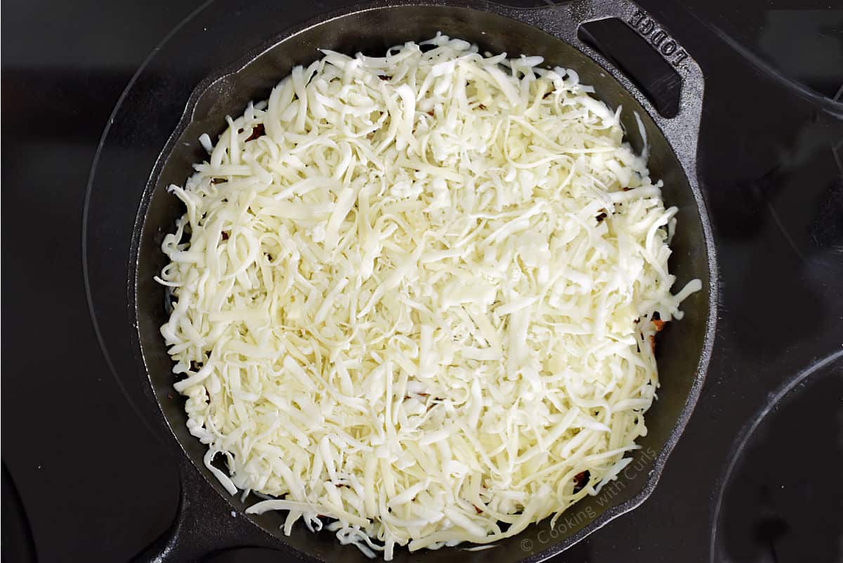 Shredded white cheese in a cast iron skillet.