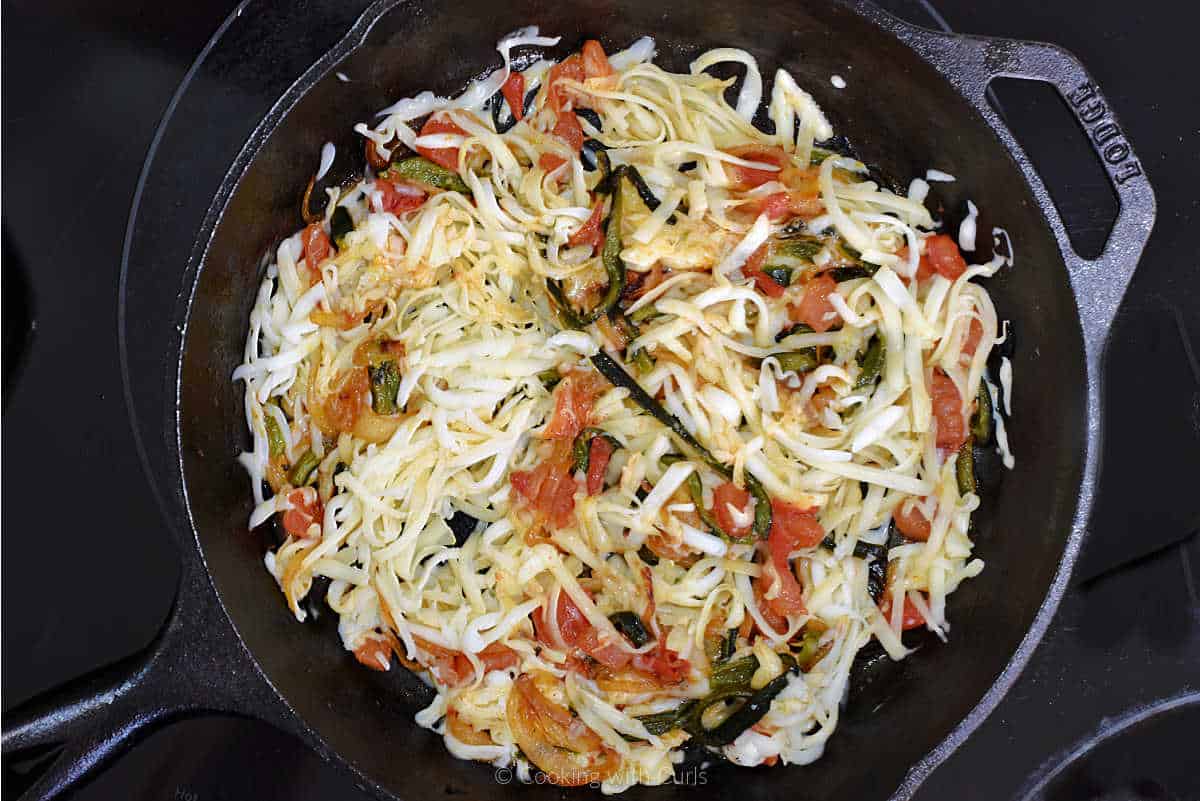 Shredded white cheese, poblano peppers, onion, and tomato mixed in skillet.