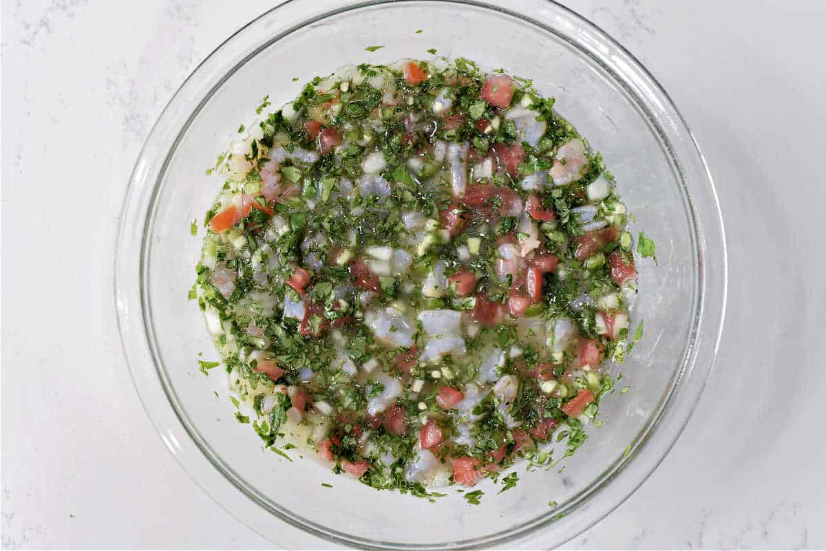 Raw shrimp ceviche in a glass bowl submerged in lime juice, cilantro, and chopped vegetables.