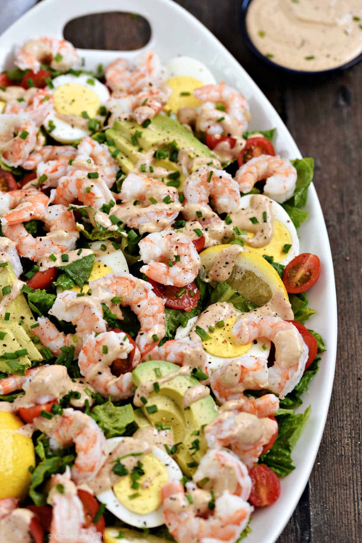 An oval platter with lettuce, shrimp, avocado, tomato, and eggs.
