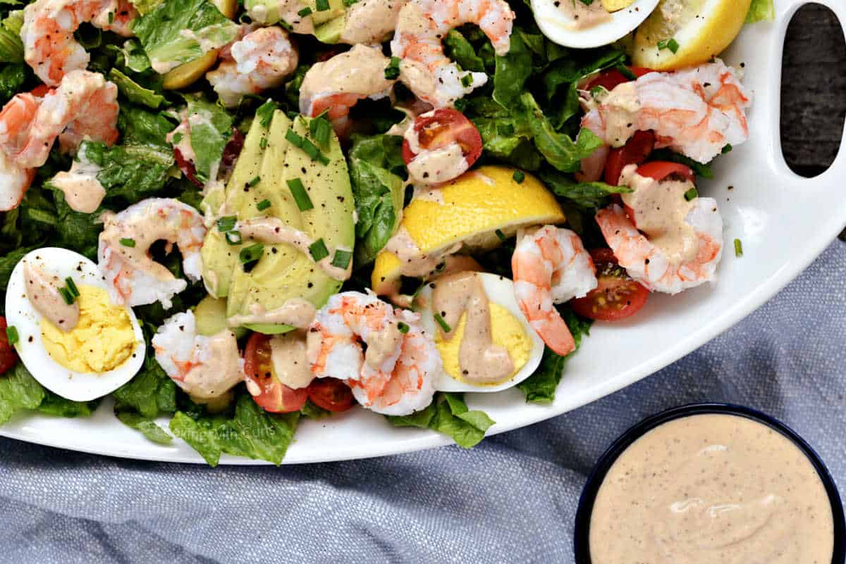 Shrimp Louie salad on a platter with dressing in a small bowl on the side.