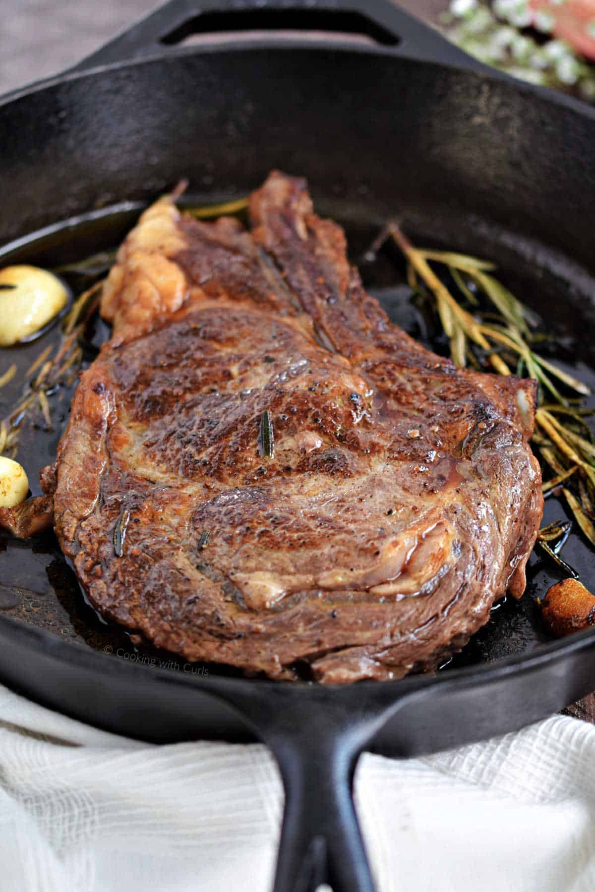 Pan-seared ribeye steak cooked in a cast iron skillet with garlic and herbs.
