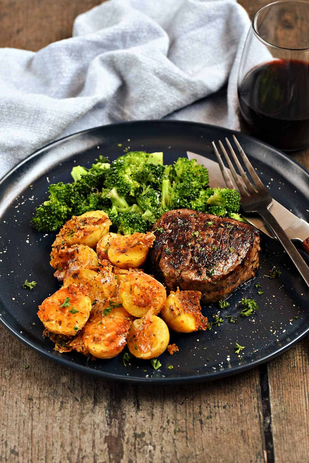 Crispy parmesan roasted potatoes on a plate with a steak and steamed broccoli florets.