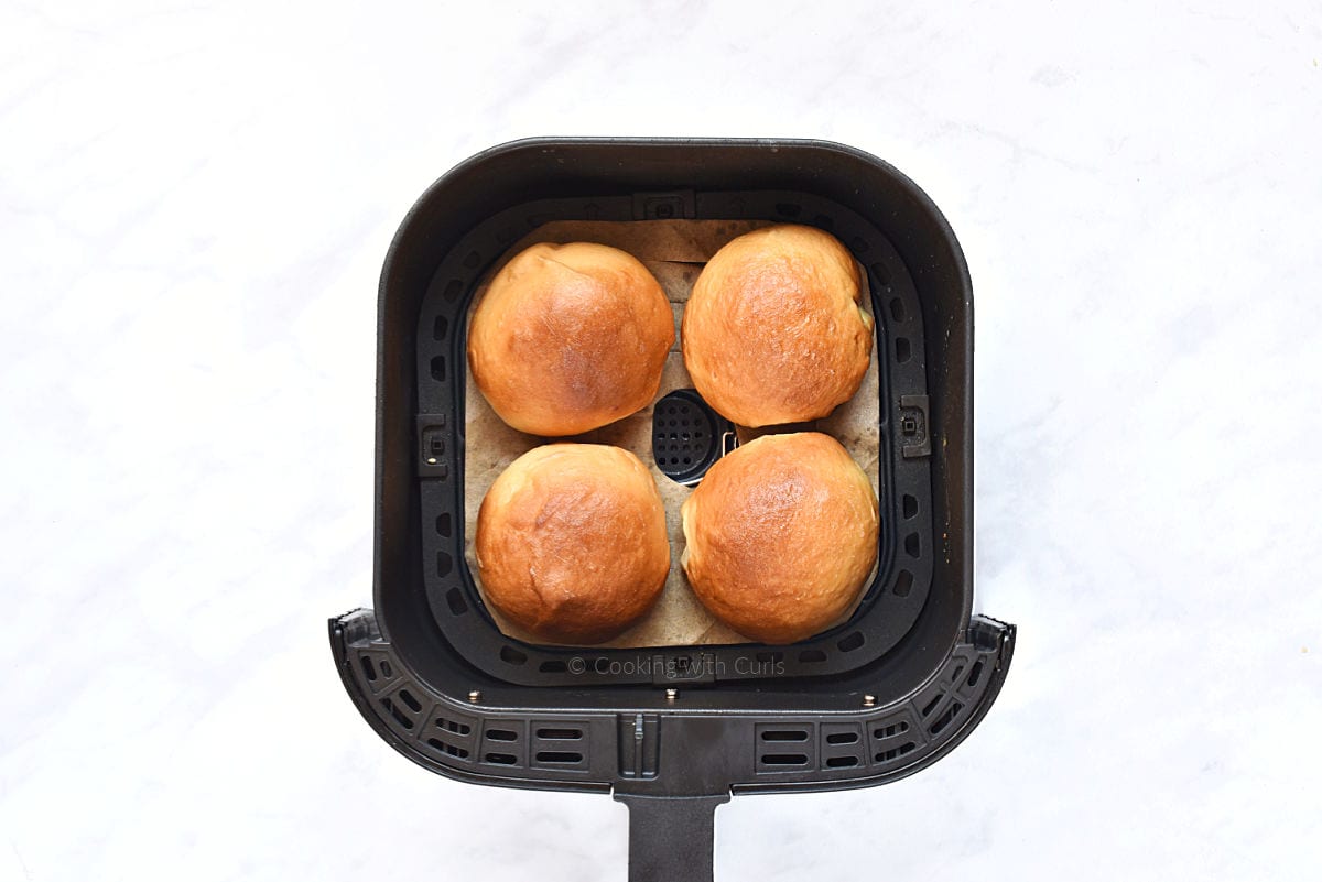 Four baked hamburger buns in air fryer basket.