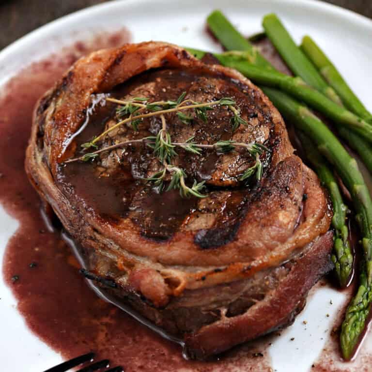 Grilled bacon wrapped filet mignon steak with red wine sauce and asparagus spears.