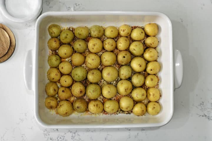 Baby potato halves on parmesan cheese mixture in baking dish.