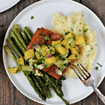 Salmon filet topped with mango avocado salsa on a bed of mashed potatoes and asparagus spears.