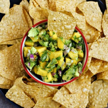 Diced mango, avocado, cilantro, and jalapeno in a bowl surrounded by tortilla chips.