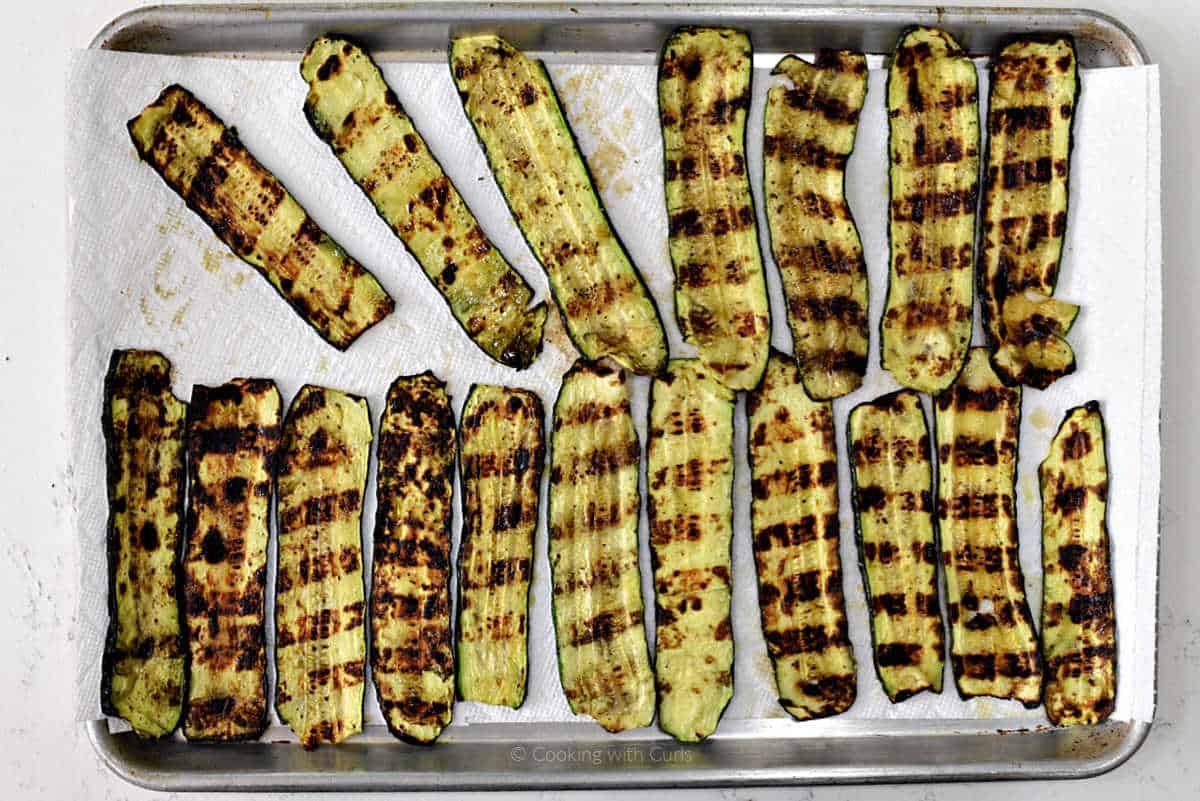 Grilled zucchini slices on paper towel lined baking sheet.