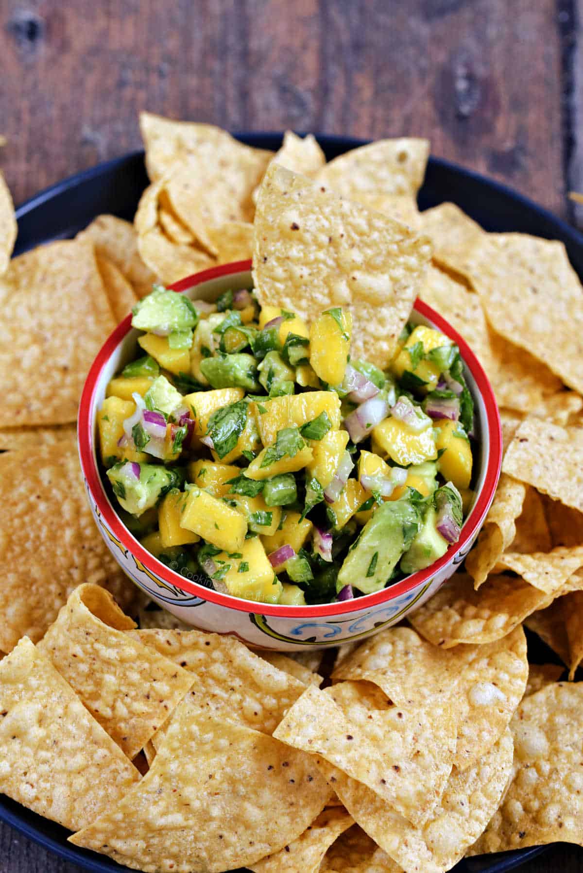 Easy mango avocado salsa in a small bowl surrounded by tortilla chips on a large plate.