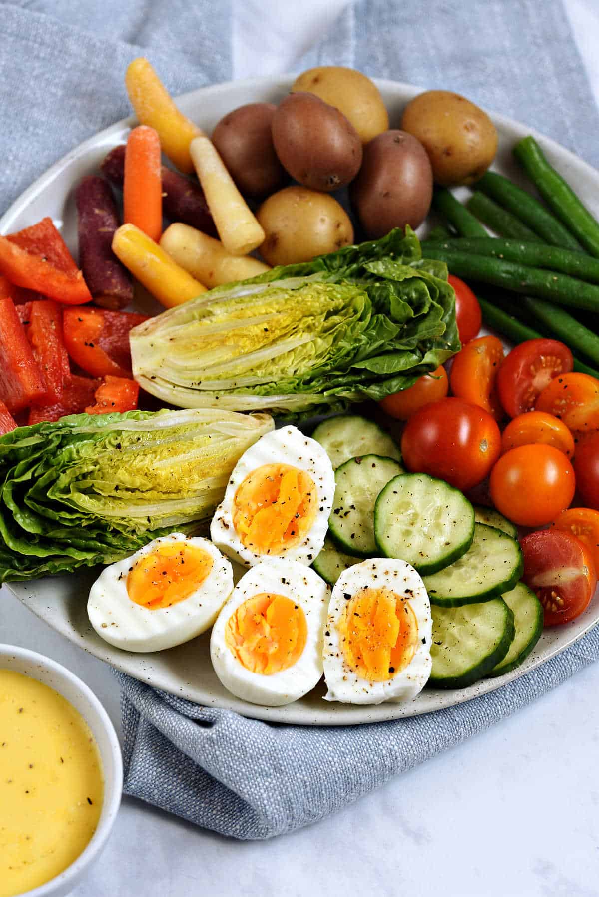 A platter of fresh vegetables and hard boiled eggs with a small bowl of aioli on the side.