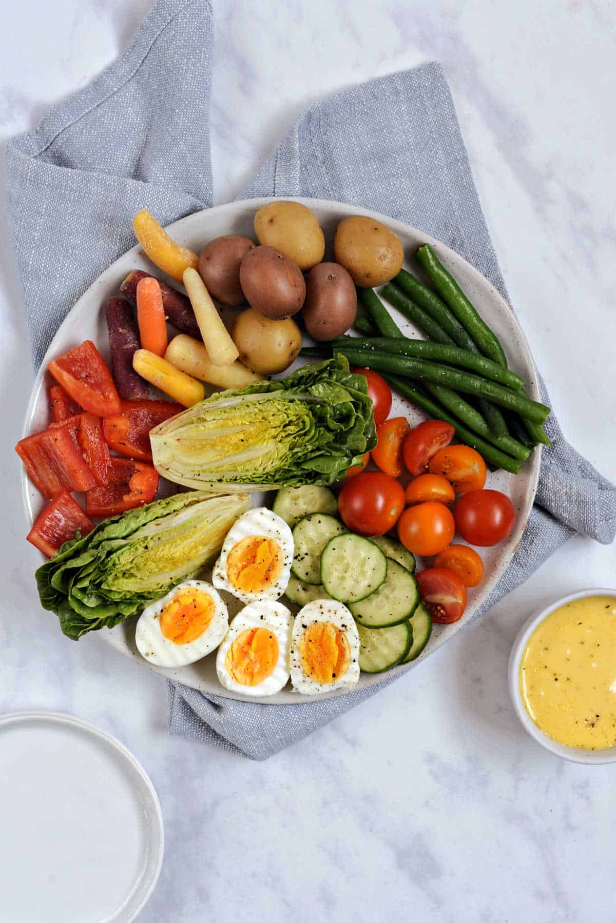 A platter filled with green beans, potatoes, hard boiled eggs, and other seasonal vegetables and a small bowl of aioli.