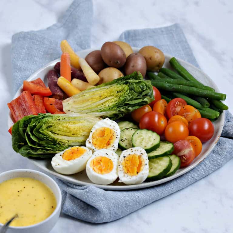 A platter of fresh vegetables and hard boiled eggs with a small bowl of aioli on the side.