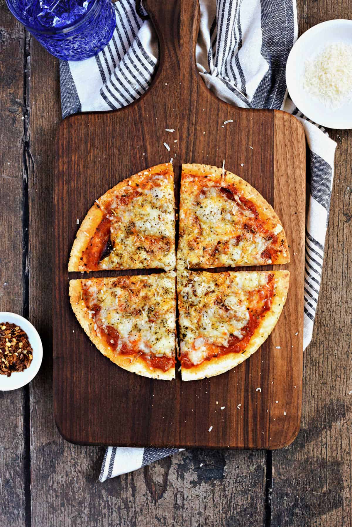 Cheesy tortilla pizza cut into quarters on a wooden cutting board.