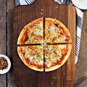 Cheesy tortilla pizza cut into quarters on a wooden cutting board.