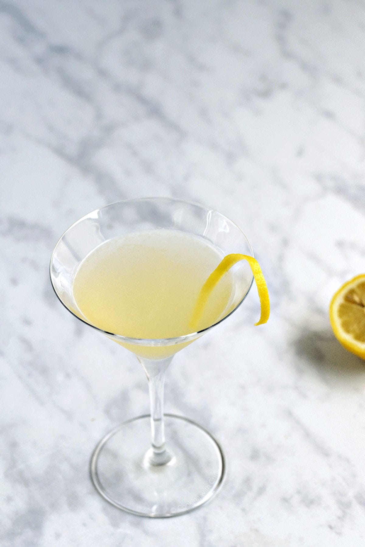 A yellow cocktail in a martini glass with a lemon twist.