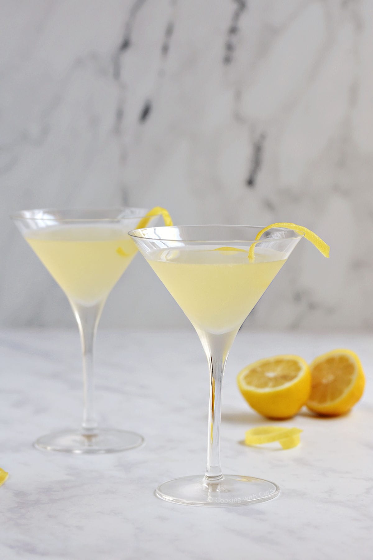 Two yellow cocktails in martini glasses with a lemon twist.