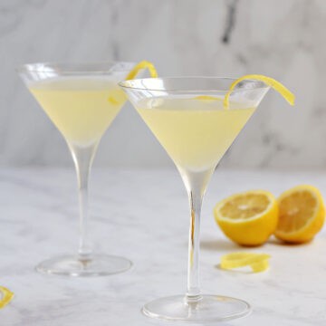 Two yellow cocktails in martini glasses with a lemon twist.